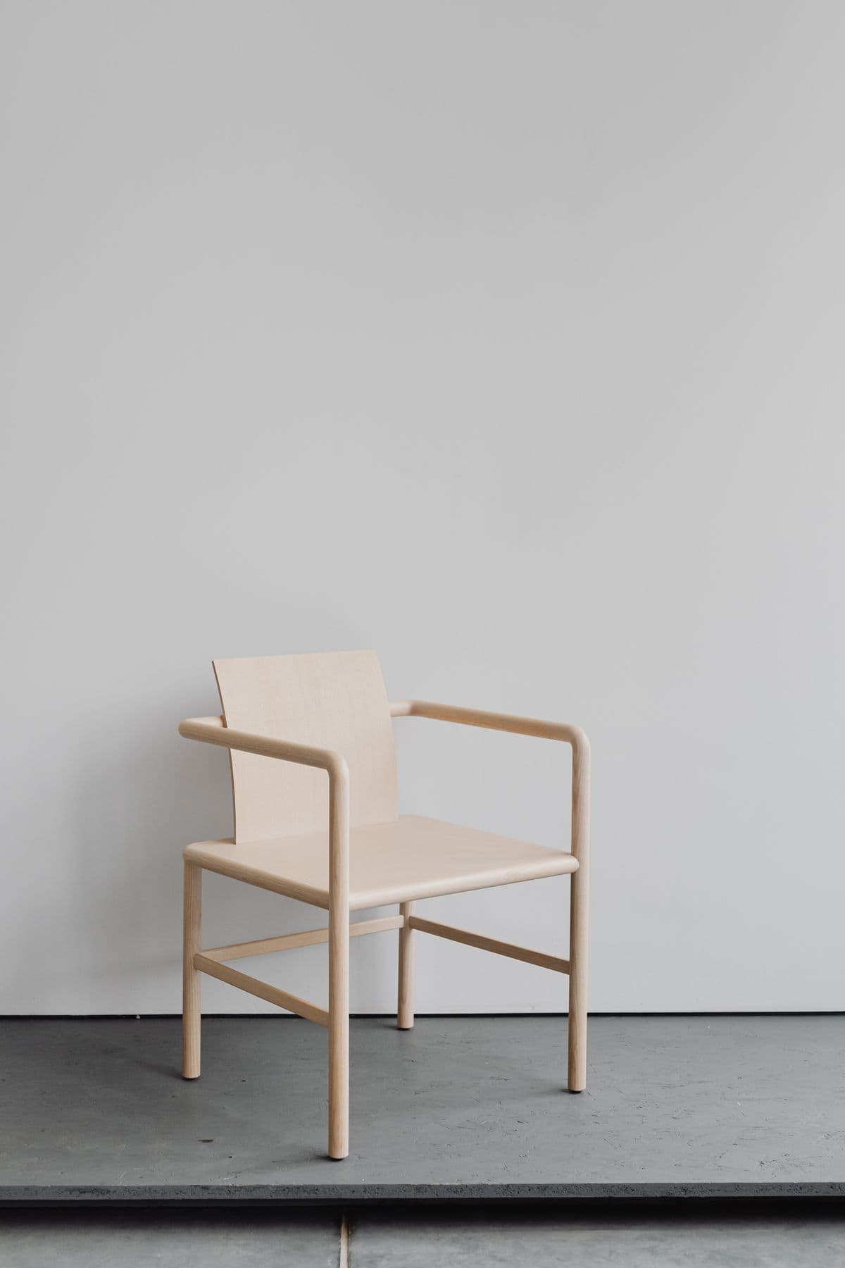 A pale timber armchair against a light grey wall.
