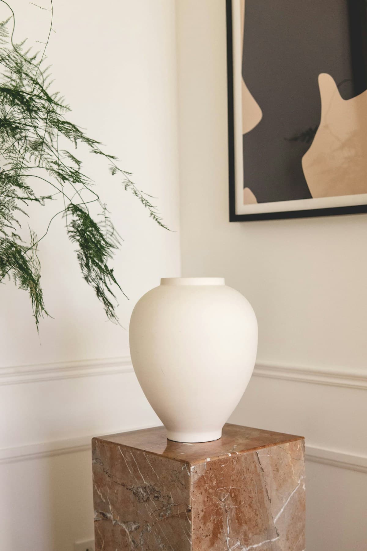 An ivory ceramic vase on a stone pedestal in a softly lit room.