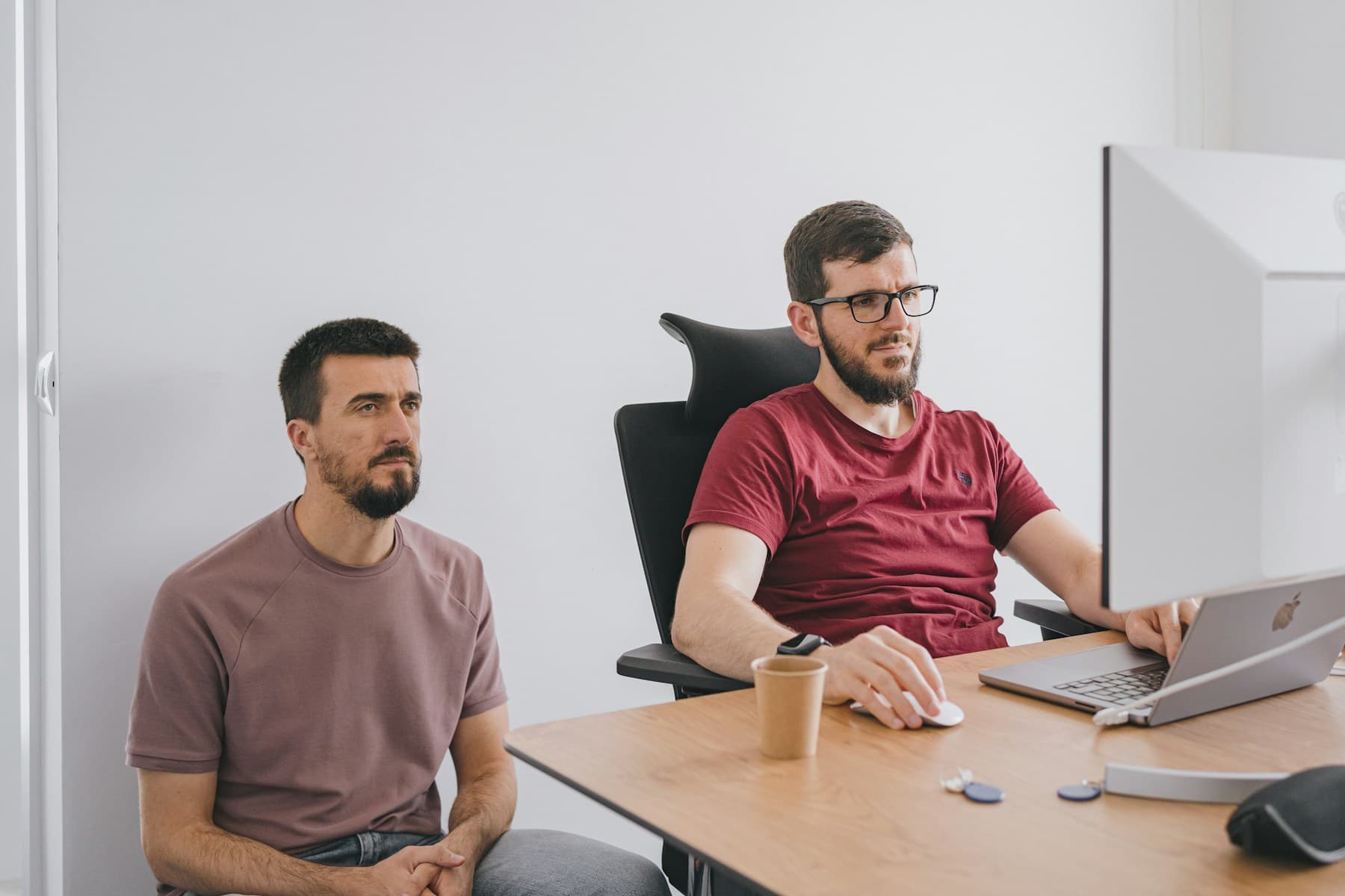 Two men reviewing work together at a desktop computer.