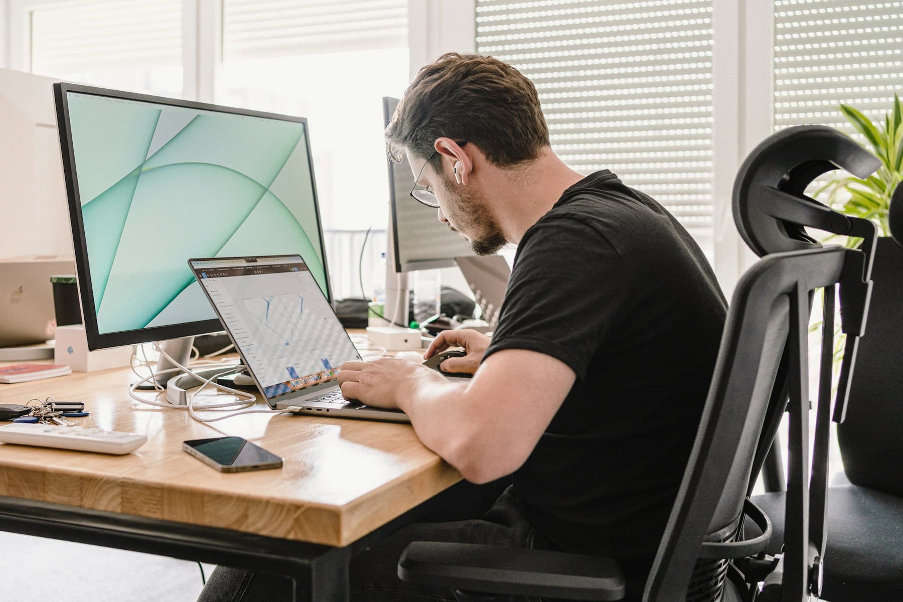 A man working on a laptop beside a desktop monitor.