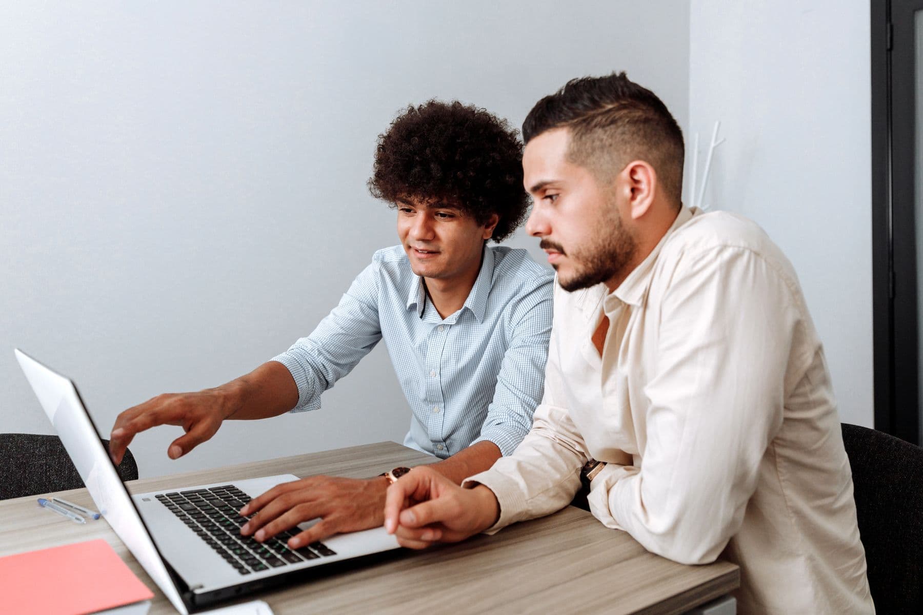 Two men working side by side on a laptop at a meeting table.
