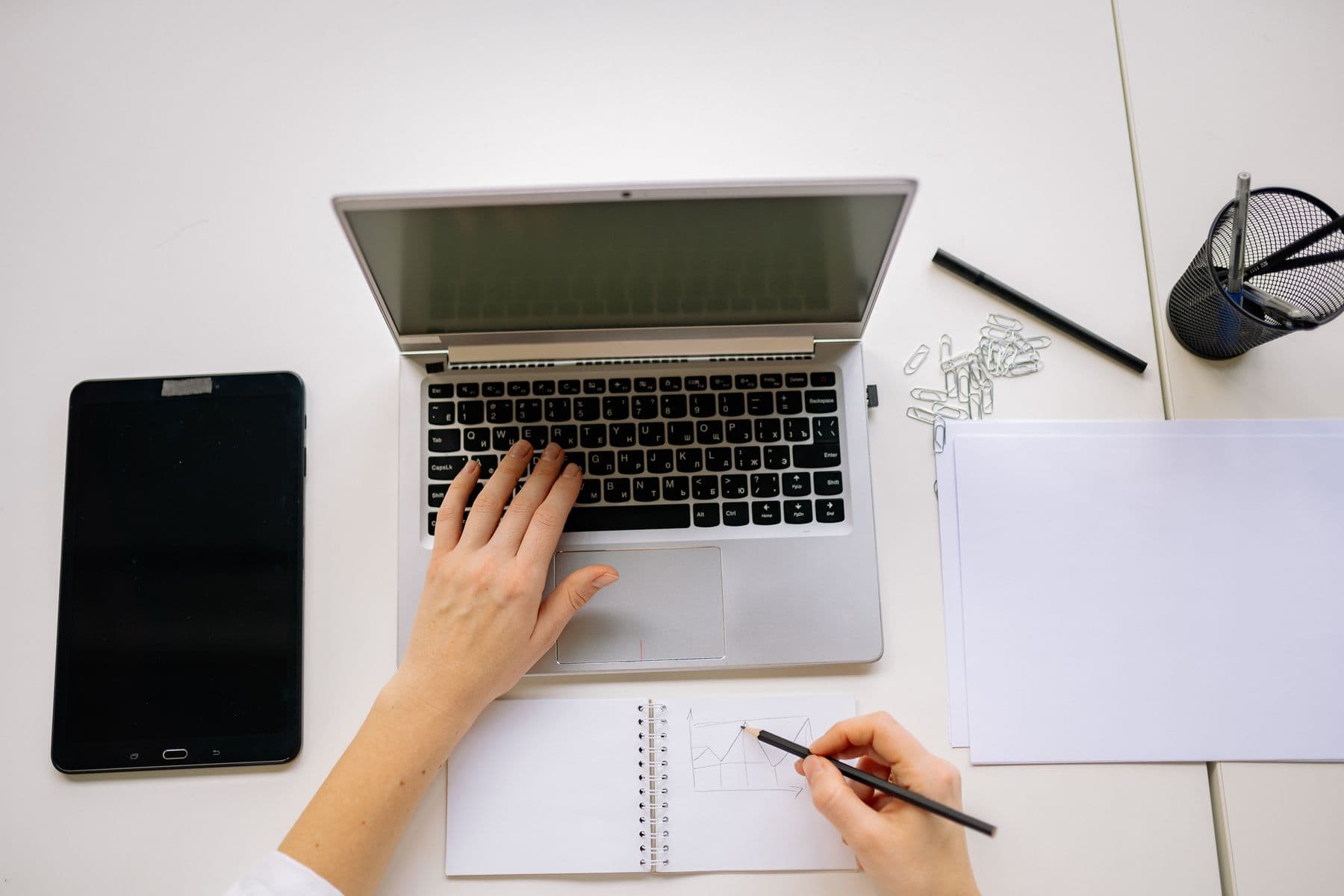 An overhead view of hands drawing a chart in a notebook beside a laptop.